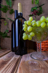 Obraz premium Two bottles of red and white wine on a wooden table with a bunch of grapes.