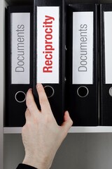 Reciprocity. File Folder is taking by a hand from office shelf. Red Text is on the label of the...