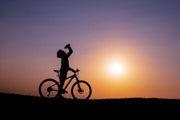 Fototapeta na wymiar break time for the cyclist, drinking water and enjoying the sunrise