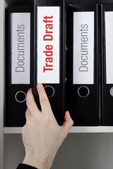 Trade Draft. File Folder is taking by a hand from office shelf. Red Text is on the label of the...