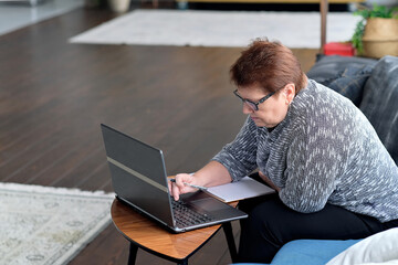 Fototapeta na wymiar Senior woman using laptop for websurfing. The concept of senior employment, social security. Mature lady sitting at work typing a notebook computer in an home office.