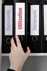 Utilization. File Folder is taking by a hand from office shelf. Red Text is on the label of the...