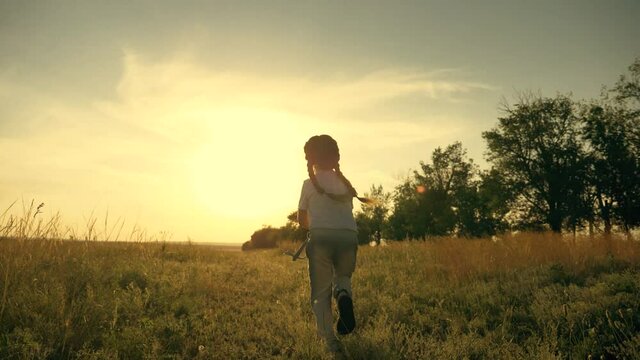 A happy, carefree child runs through a green field, enjoys nature, fresh air. A girl at sunset on a summer day holding a net, a child's toy for catching insects.
