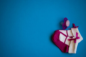 Small baby purple socks and pacifier on blue background with copy space