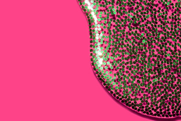 transparent liquid with green glitter pouring over a pink background