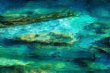Crystal clear glacial melting water running over smooth rocks and pebbles in a wild forest river. Close up.