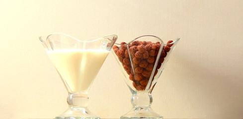     two glass cups with chocolate corn balls and milk. cereal with milk                           