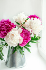 Bouquet of beautiful peonies on the windowsill. Pink and white peonies in a tin jug. Soft focus