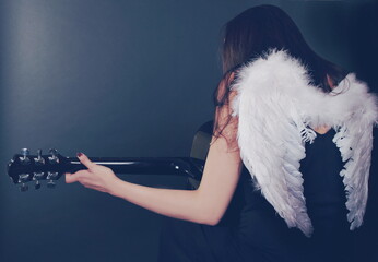 Girl with angel wings playing guitar, view from the back, dark mood of rock