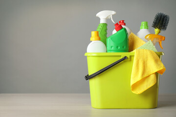 Bucket with cleaning products and tools on grey table. Space for text