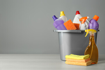 Bucket with cleaning products and tools on grey table. Space for text
