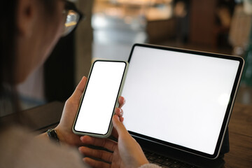 Cropped shot of young woman hands using smart phone while sitting in front of desktop of tablet.