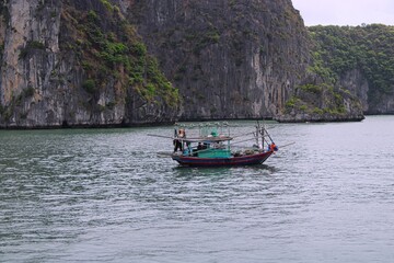 Fototapeta na wymiar Fishing boat in between the stunning rocks of nature heritage Halong bay in Vietnam