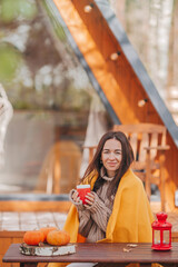 Happy young woman drinking coffee sitting at the wooden table outdoors