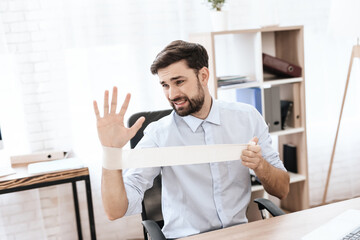 A man with beard sits at table and bandages hand.