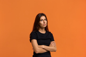 Obraz premium It is a big problem for me. Contemplative caucasian woman in black t-shirt keeps hands crossed over chest, ponders on how to solve situation, looking for solution. Isolated over an orange background.