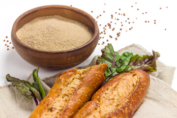 Buckwheat seeds and flour in ceramic bowl, homemade french baguette on sackcloth isolated on white background. Organic healthy food concept