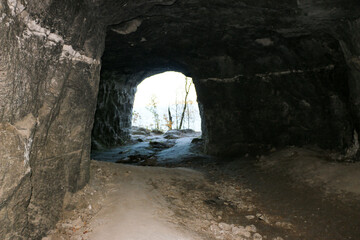 exit from cave, with natural stone walls. Exit from mountain to sunlight that illuminates trees and nature. Natural tunnel overlooking landscape. Trees and plants, framed from exit from stone adit.