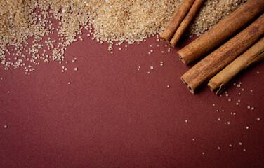 Cinnamon sticks with brown sugar on dark red background with blank text space top view