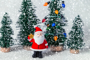 Christmas image with a toy Santa Claus and miniature fir trees on a shiny paper background