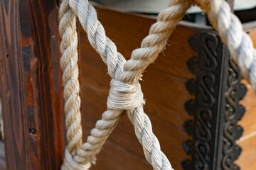 Thick rope ropes, intertwined crosswise, hang on wooden railings, decorative fence along the alley in the Park for recreation. Metal rings and large strong knots on a stone background