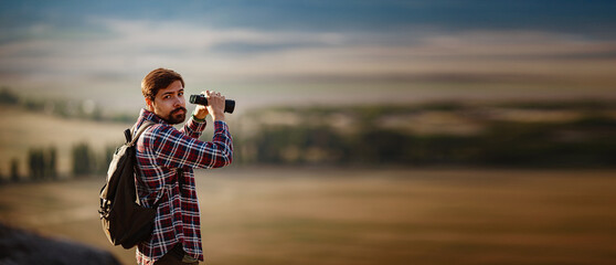 Guy looking at binoculars in hill. man in t-shirt with backpack.