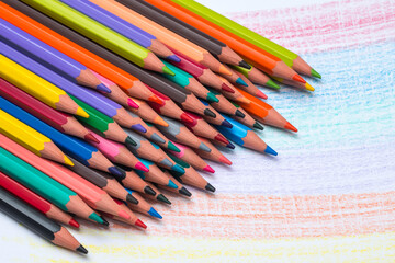 Obraz premium A stack of color pencils crayons lying on hand drawing white sheet of paper. School supplies. Educational concept