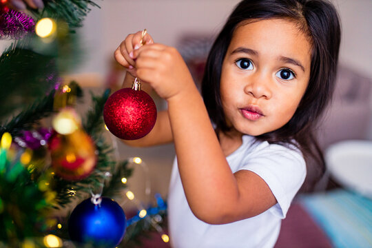 mixed race little cute girl decorating a christmas tree in the xmas morning in bedroom and wishing a wish