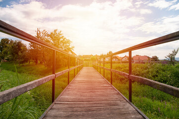 Empty wooden bridge in village, sunset sky. Countryside landscape