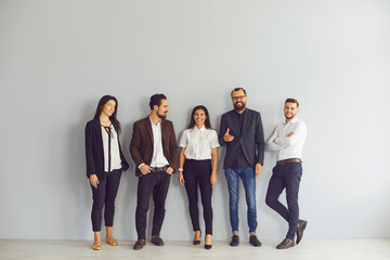 Group of happy young business people standing near studio wall looking at camera