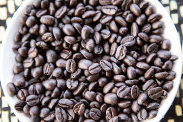 Dry group of black coffee bean in a white bowl.