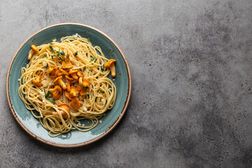 Pasta spaghetti with wild forest mushrooms chanterelles on plate. Seasonal autumn dish on rustic concrete background from above. Meal with aromatic fall chanterelles. Food background, copy space