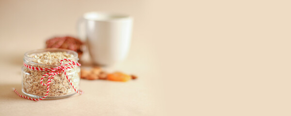 Homemade oatmeal flakes in a glass open jar with dried apricots, nuts on a beige background with copyspace