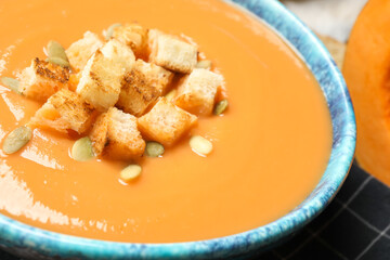 Tasty creamy pumpkin soup with croutons and seeds in bowl on table, closeup