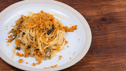 Spaghetti alla carrettiera, pasta with onions and breadcrumbs in a plate close-up on a rustic wooden table, top view, copy space