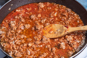 Cooking tortiglioni with onion and sausage stew, pasta with sausage sauce with onions and tomato paste - cooking onion and sausage stew in a pan, close-up