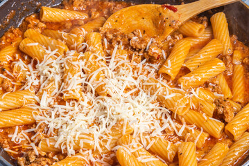 Cooking tortiglioni with onion and sausage ragout, pasta with sausage sauce with onion and tomato paste - tortilloni al dente with onion and sausage ragout and grated cheese in a pan, close-up