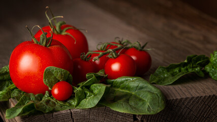 Ripe bunches of tomato, green spinach leaves on a wooden table