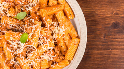 Cooking tortiglioni with onion and sausage ragout, pasta with sausage sauce with onions and tomato paste, sprinkled with tertum cheese on a plate on a rustic wooden table, top view, copy space