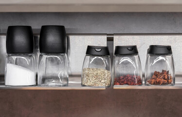 Glass jars with various spices and seasonings on the kitchen shelf.