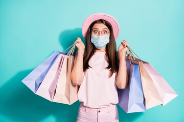 Portrait of delighted girl fashionista carrying bags wear safety mask isolated green turquoise color background