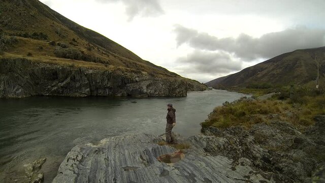 A fly fisherman casting in strong wind on a wet day on a rocky Ahuriri River