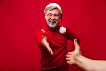 Fototapeta premium Excited old man posing with smile in christmas day. Studio photo of happy grey-haired grandpa in santa claus costume.