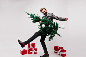Full-length shot of excited young man dancing before new year party. Glad handsome guy holding green christmas tree.