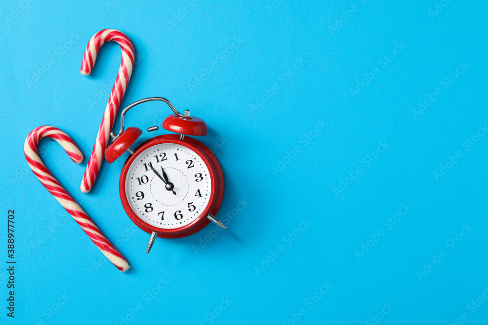 Poster alarm clock and candy canes on light blue background, flat lay with space for text. new year countdo
