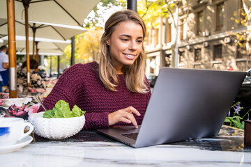 Young woman working on laptop computer at restaurant, eating break during work