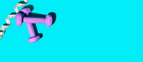 Top view of purple dumbbells and tape measure on a blue background. Copy space, banner. Overweight concept, fitness, active lifestyle, sports and health