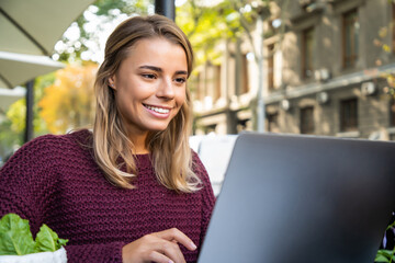 Working outdoors. Beautiful young woman working on laptop and smiling while sitting in cafe