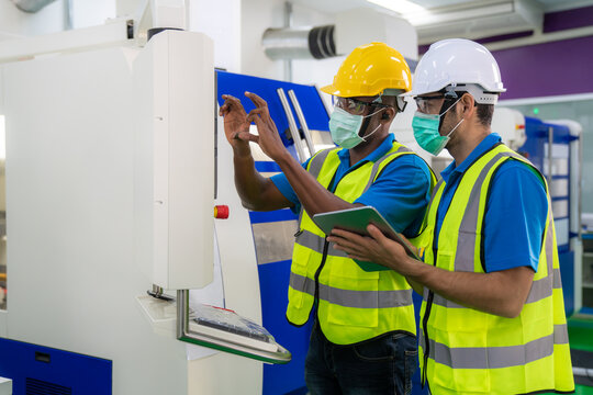 Asian Industrial Engineers And Worker In Hard Hats Discuss Product Line While Using Digital Tablet In Cnc Milling Cutting Machine In A Heavy Industry Manufacturing Factory.