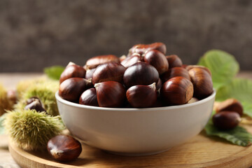 Fresh sweet edible chestnuts in bowl on wooden board